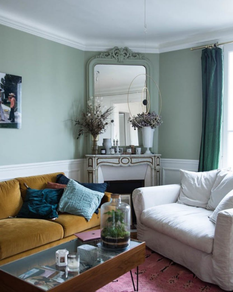 Image via @thesocialitefamily, sage green walls with velvet mustard yellow sofa.